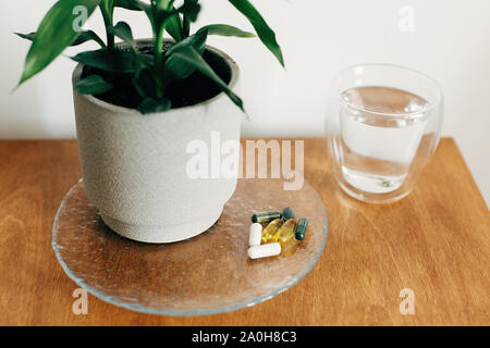 Omega 3, Spirulina, Chlorophyll, Magnesium Kapseln und Glas Wasser auf Holztisch. Morgen vitamin Pillen. Nahrungsergänzungsmittel, biologisch aktive Stockfoto