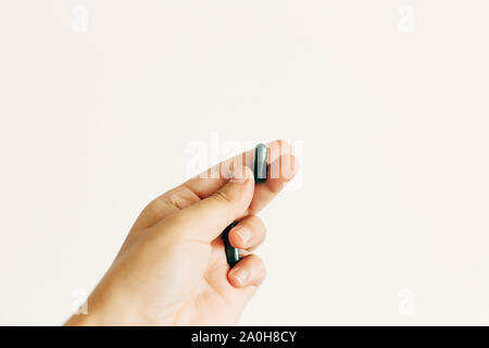 Hand mit Spirulina Kapsel auf weiße Wand im Hintergrund. Morgen vitamin Nährstoff Pille. Nahrungsergänzungsmittel. Gesundheit Unterstützung und Behandlung. Biologicall Stockfoto