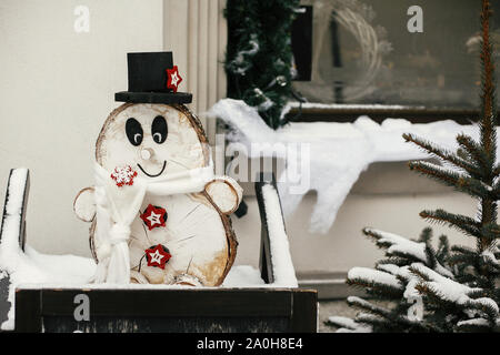 Weihnachten rustikalen Straße eingerichtet. Stilvolle weihnachten Holz Schneemann im rustikalen Weihnachtsbaum bei Store Front im Holiday Markt in verschneite Straße der Stadt. Raum Stockfoto