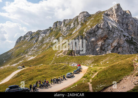 Panoramaaussicht auf dem Berg Buconig und Mangart Straße, Mangartska cesta, mit Parkplatz, Autos, Motorrädern und Menschen. Von Mangart Sattel genommen. Slowenien. Stockfoto