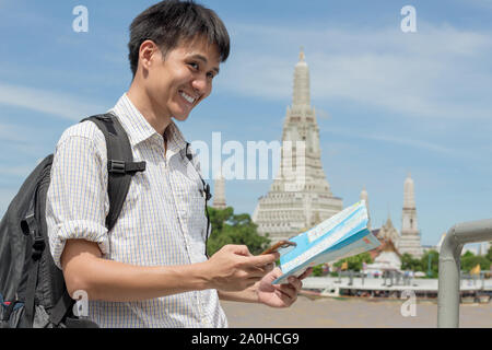 Mann mit einem Plaid Shirt Holding ein Smartphone mit einer Karte bei Wat Arun in Thailand. Stockfoto