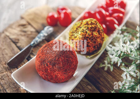 Käse belper Knolle, die in den Gewürzen roten und schwarzen Pfeffer und Kräutern der Provence. Kleine hausgemachte Kugeln von Käse Belper. Delikatesse runde kleine Käse mit Schwarz Stockfoto