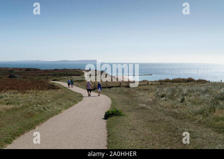 Die Isle of Wight gesehen von Hengistbury Head, mit Wanderern im Vordergrund genießen Sie den Spätsommer Sonnenschein und herrlichem Ausblick. Stockfoto