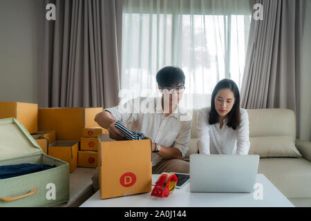 Asiatische junge Paar verkaufen on-line über einen Computer und helfen, um das Kontrollkästchen zu aktivieren, um E-Mails in Wohnzimmer im Haus zu senden. Small Business Start Stockfoto