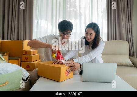 Asiatische junge Paar verkaufen on-line über einen Computer und helfen die Bestellung des Kunden in Kartons zu packen Mail im Wohnzimmer im Haus zu senden. Kleine Stockfoto