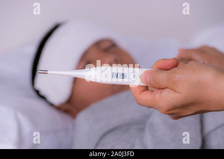Frau hand mit einem Thermometer die Temperatur auf einer verschwommenen Hintergrund eines Jungen zu messen. Gesundheit und medizinische Konzept. Stockfoto