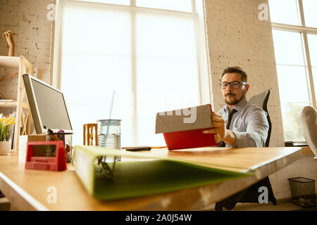 Angebote. Ein junger Unternehmer, die im Büro, neue Arbeit. Junge männliche Mitarbeiter bei der Verwaltung nach der Promotion. Seriöse Erscheinungsbild, zuversichtlich. Business, Lifestyle, neues Leben Konzept. Stockfoto