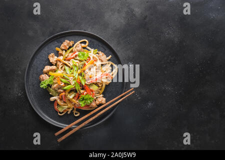 Udon unter Rühren braten Schüssel Nudeln mit Schweinefleisch und Gemüse auf schwarzen Stein Hintergrund. Asiatische Küche. Ansicht von oben. Kopieren Sie Platz. Stockfoto