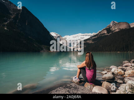 Frau sitzt am Ufer von Lake Louise in den Rocky Mountains. Stockfoto