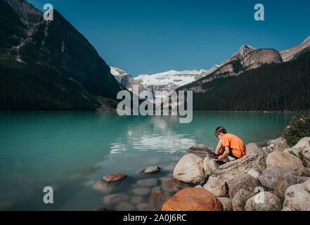 Junge Junge sitzt auf felsigen Ufer von Lake Louise in den Bergen. Stockfoto