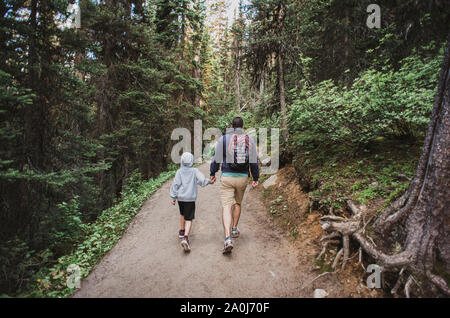 Vater und Sohn halten sich an den Händen, als sie auf einem Pfad in den Wald wandern. Stockfoto