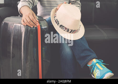 Weibliche Reisende sitzt mit Reisetasche und Strohhut auf leder Sofa am Flughafen. Travel Concept. Stockfoto