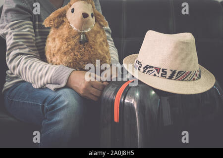 Weibliche Reisende mit ihrem Schaf doll, Reisetasche und Strohhut während am Flughafen warten. Travel Concept. Stockfoto