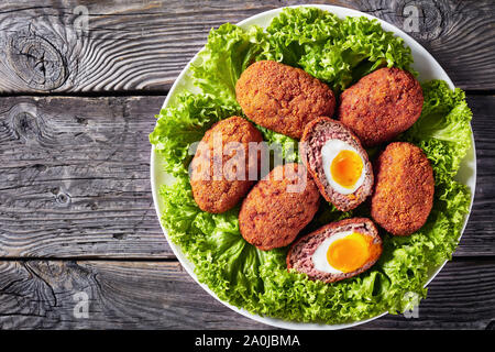 Close-up von Scotch Eier, weich gekochte Eier mit flüssig Eigelb in Hackfleisch, paniert und frittierte gewickelt, mit Salat auf einem Teller serviert auf einem alten Woo Stockfoto