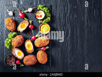 Scotch Eier, weich gekochte Eier mit flüssig Eigelb in Hackfleisch gewickelt, serviert mit Mayonnaise und Senf auf einen schwarzen Stein Fach, Ansicht von oben, flatl Stockfoto