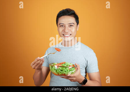 Happy asiatischer Mann das Essen von frischem Gemüse Salat auf oange Hintergrund isoliert Stockfoto