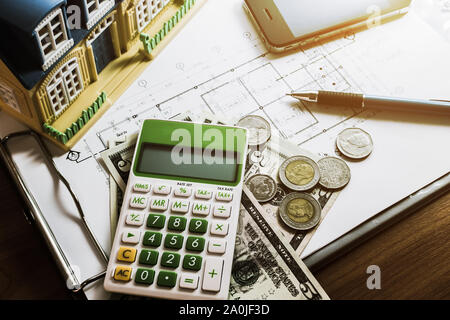 Die Investitionen für den Bau mit einem limitierten Budget, Bauplan, pen, Geld, Modell, Haus, Smart Phone und Taschenrechner auf hölzernen Tisch unter Licht Stockfoto