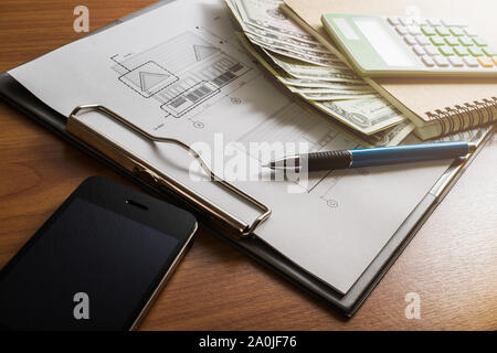 Die Investitionen für den Bau mit einem limitierten Budget, Bauplan, Stift, Geld, Notebook, Smartphone und Rechner auf hölzernen Tisch Stockfoto