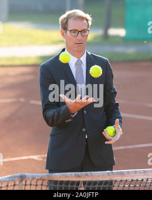Unternehmer im dunklen Anzug jonglieren mit Tennisbällen auf Tennisplatz Stockfoto