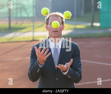 Unternehmer im dunklen Anzug jonglieren mit Tennisbällen auf Tennisplatz Stockfoto
