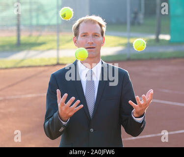 Unternehmer im dunklen Anzug jonglieren mit Tennisbällen auf Tennisplatz Stockfoto