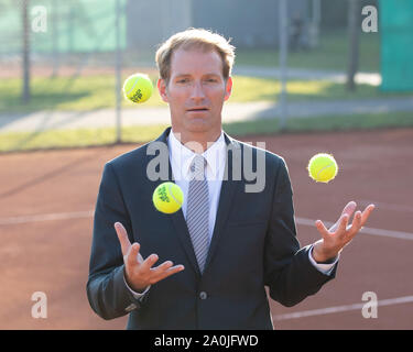 Unternehmer im dunklen Anzug jonglieren mit Tennisbällen auf Tennisplatz Stockfoto