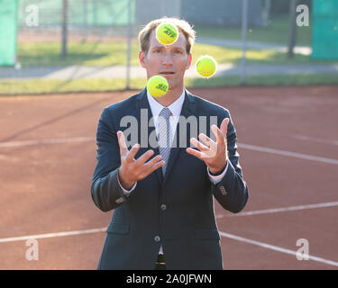 Unternehmer im dunklen Anzug jonglieren mit Tennisbällen auf Tennisplatz Stockfoto