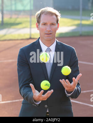 Unternehmer im dunklen Anzug jonglieren mit Tennisbällen auf Tennisplatz Stockfoto