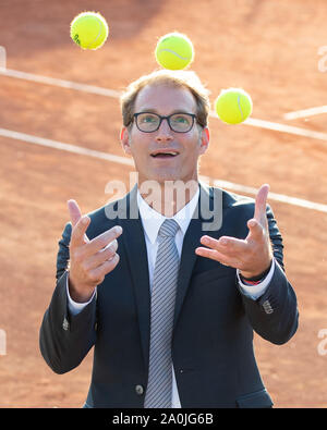Ansicht von lächelnden Geschäftsmann in dunklen Anzug jonglieren mit Tennisbällen auf Tennisplatz Stockfoto