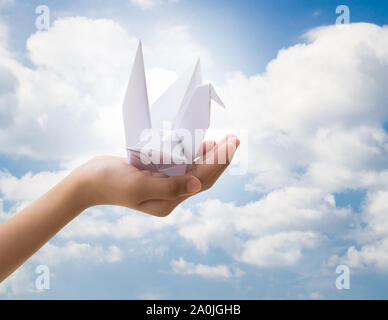 Hand des kleinen Mädchens holding Vogel Papier origami mit bewölkt blauer Himmel, Freiheit Konzept Stockfoto