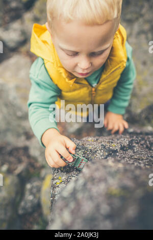Toddler Boy mit Spielzeug spielen auf einem Felsen. Kleines Kind zu Fuß auf Rocky Mountains. Stockfoto