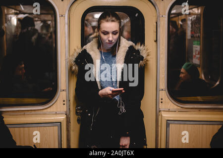 Junge Frau hört Musik auf das Telefon während der Fahrt in der U-Bahn Stockfoto