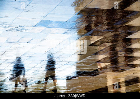 Blurry abstrakte Schatten silhouette Reflexionen von zwei Menschen zu Fuß auf nasser Straße Bürgersteig Stockfoto