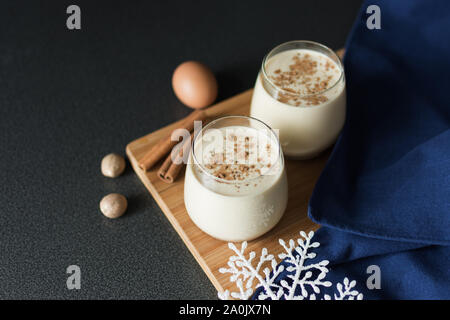 Frische Eierlikör mit Zimt und Muskatnuss für Weihnachten mit Weihnachtsschmuck auf dunklem Hintergrund, Low Key. Stockfoto