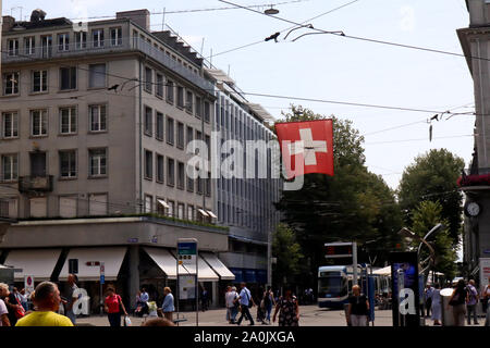 Zürich, Schweiz, 19. Juli 2019: Flagge der Schweiz hängen an mitten auf der Straße, Verkehr und Alltag in Paradeplatz in Zürich Stockfoto