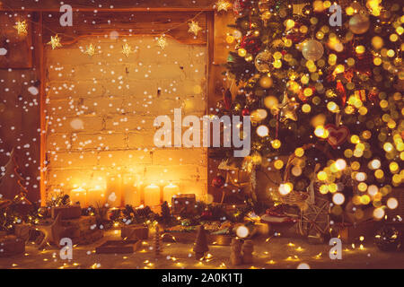 Zauberhafte Weihnachten Zusammensetzung, dekoriert mit Kamin mit Holz- Kaminsims, beleuchtete Weihnachtsbaum mit Flitter Ornamente, Sterne, Lichter, Kerzen, getönt, Schnee, Imitation, Bokeh, selektiver Fokus Stockfoto