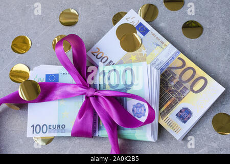 Euro-banknoten auf einem Stapel mit violetten Bogens. Geschenk, Prämie oder Belohnung Konzept. Selektiver Fokus Stockfoto