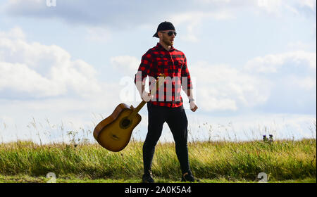 Landhausstil. Sommer Urlaub. Wandern Song. Inspiriert land Musiker. United mit der Natur. Stattlicher Mann mit Gitarre. Country Music Konzept. Gitarrist Land Sänger stand im Feld Himmel Hintergrund. Stockfoto