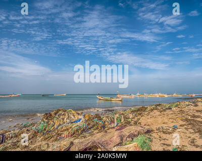 Senegal, Afrika - Januar 26, 2019: Viel Plastiktüten am Ufer des Ozeans. Umweltverschmutzung Konzept. Bunte Fischerboote im Hintergrund. Senegal. Stockfoto