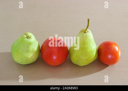 Zwei reife grüne Birnen und zwei rote Tomaten nebeneinander auf einem Holztisch isoliert Stockfoto