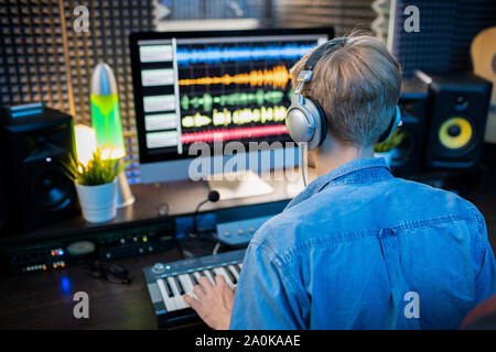 Ansicht der Rückseite des jungen Mannes in Kopfhörer Musik machen mit dem Computer Monitor Stockfoto