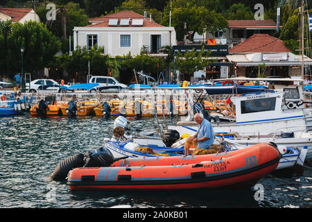 Agia Efimia, Kefalonia Insel, Griechenland - Juli, 12 2019: Eine alte griechische Fischer sitzen in einem boad und Vorbereitung einer Fischernetz für das nächste Angeln Stockfoto