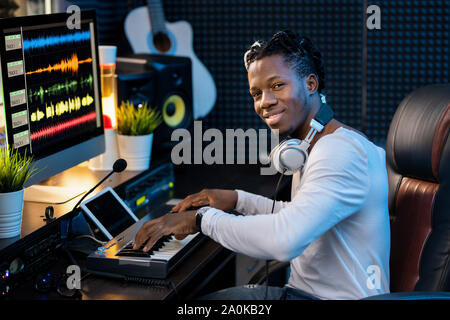 Glückliche junge Musiker mit Kopfhörer am Hals über neue Musik von Arbeitsplatz Stockfoto