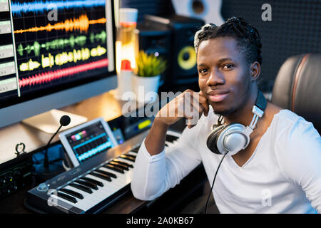 Glückliche junge lächelnd Mixed-race Mann mit Kopfhörer auf dem Hals durch Arbeitsplatz sitzen Stockfoto