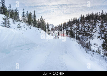 Verschneite Straße in den österreichischen Bergen. Winter Landschaft mit schneebedeckten Straße und Schneeverwehungen am Straßenrand. Pistenfahrzeug Reinigung der Straße Stockfoto