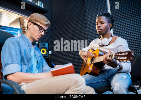 Afrikanischer Mann Gitarre spielen und singen Song, während sein Kollege Notizen zu machen Stockfoto