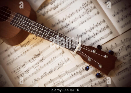 Eine kleine 4-saitige Ukulele mit Nylonsaiten liegt auf alten weißen verstreut Seiten von Noten. Stockfoto