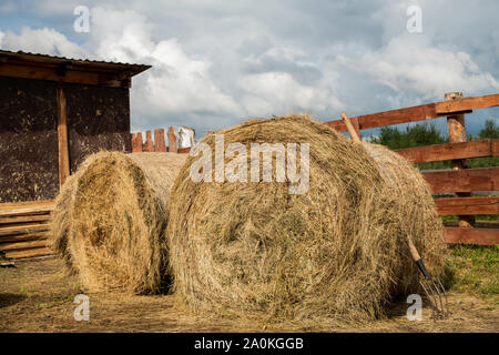 Zwei riesige gerollt Stapel von frischem Heu und Mistgabel durch die Scheune und Holzzaun Stockfoto