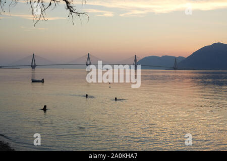 Silhouette von drei Menschen Schwimmen mit Rio - antirrio Brücke im Hintergrund bei Sonnenuntergang, Patras, Griechenland Stockfoto