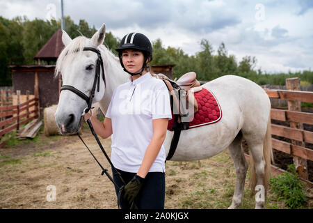 Junge Sportlerin im Reitsport Outfit stehen durch weißen reinrassigen rennpferd Stockfoto